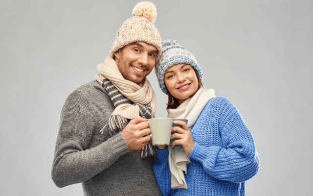 Happy couple in winter beanies holding mugs