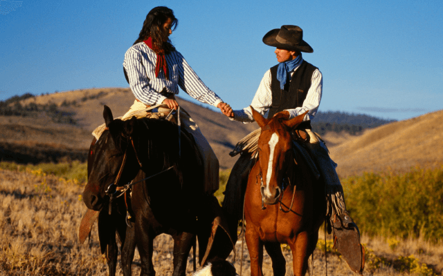 A cowboy and a cowgirl on a horseback wearing red and blue bandanas